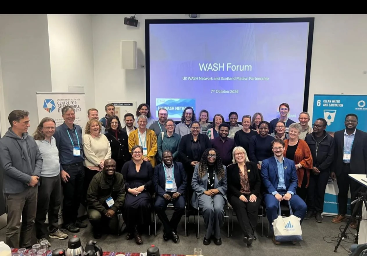 WASH Forum participants gathered beneath a screen showing the UK WASH Network and Scotland Malawi Partnership event title